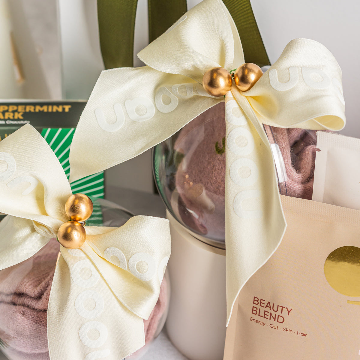 clear Christmas baubles filled with pink socks and tied with ivory bows and gold bells, beside peppermint bark. Bhone Beauty