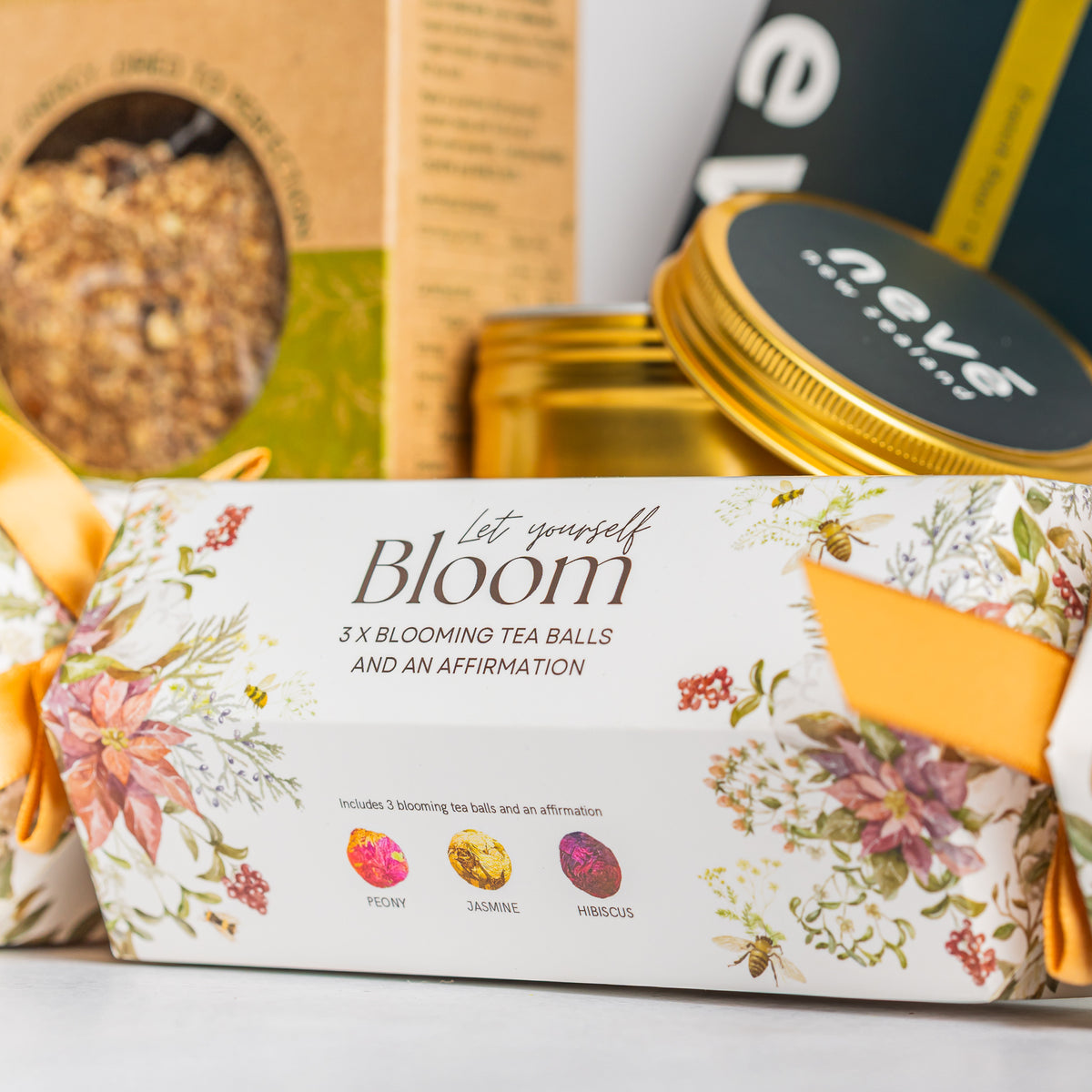 Let Yourself Bloom floral Christmas cracker containing blooming tea balls, with a gold candle tin behind
