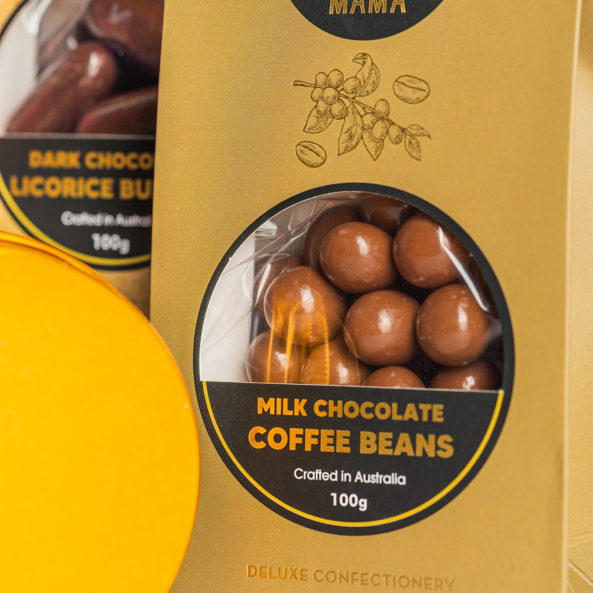 Chocamama milk chocolate coffee beans in gold packaging, with dark chocolate liquorice bullets behind.