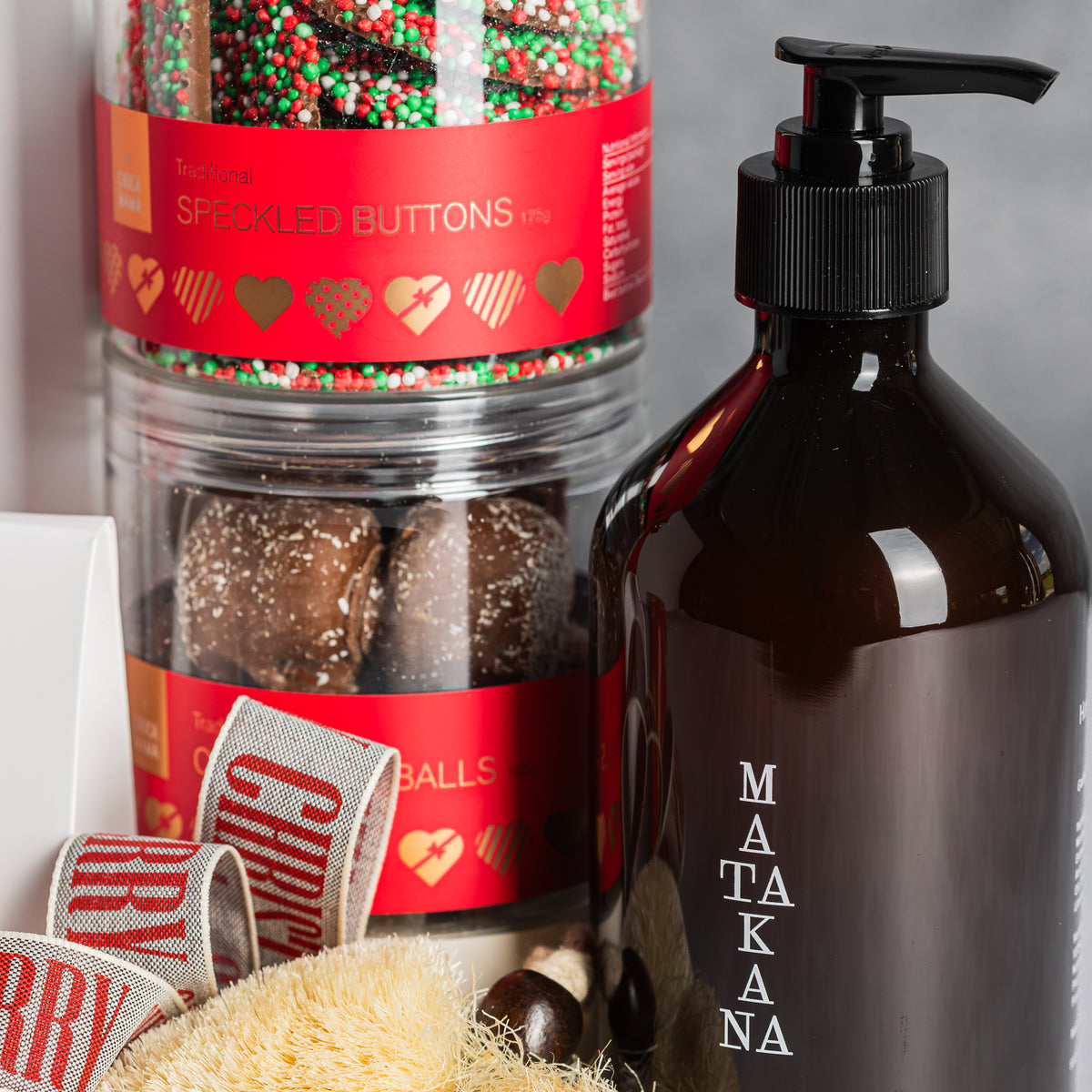 Matakana pump bottle beside stacked jars of festive chocolate buttons and chocolate balls, with a cream bath sponge