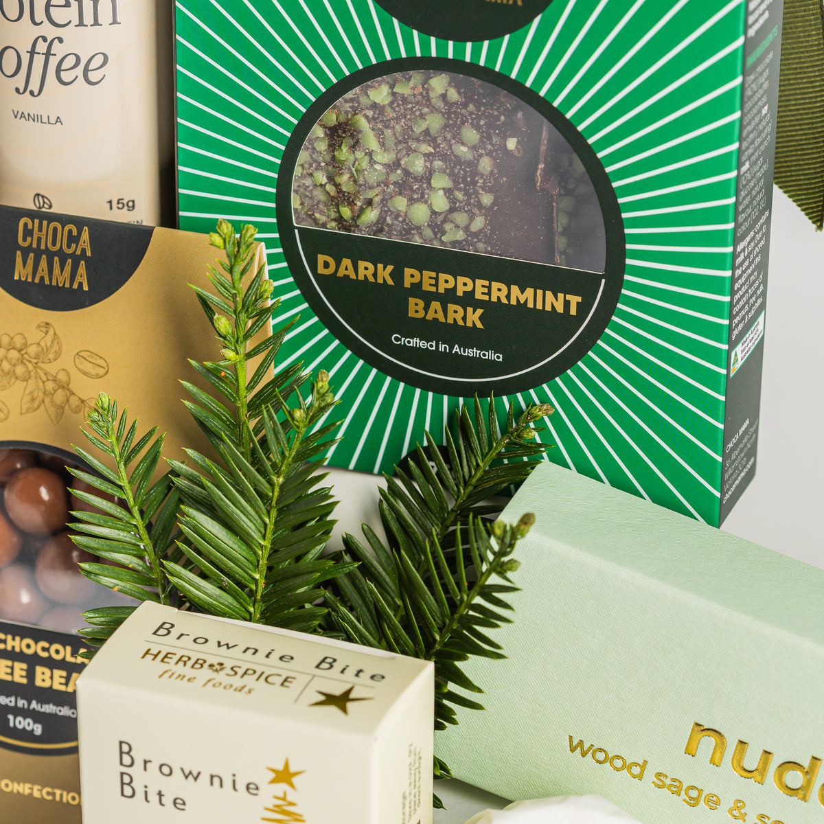 Chocamama dark peppermint bark in green packaging beside chocolate coffee beans, a brownie bite and festive greenery