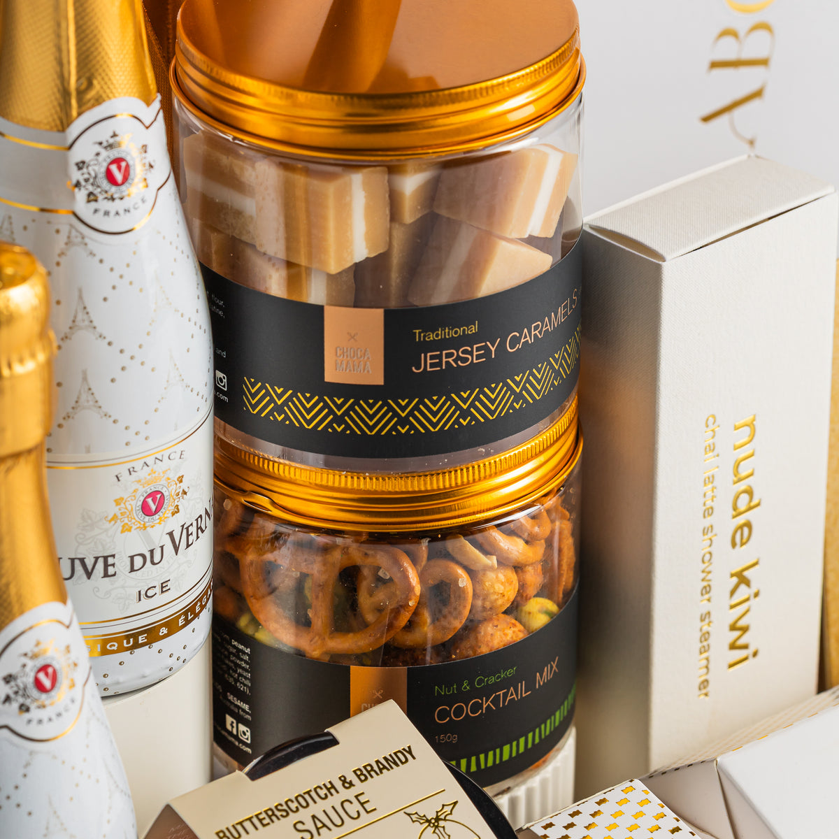 Gold-lidded jars of Jersey caramels and cocktail snack mix beside Veuve du Vernay Ice and chai latte shower steamers