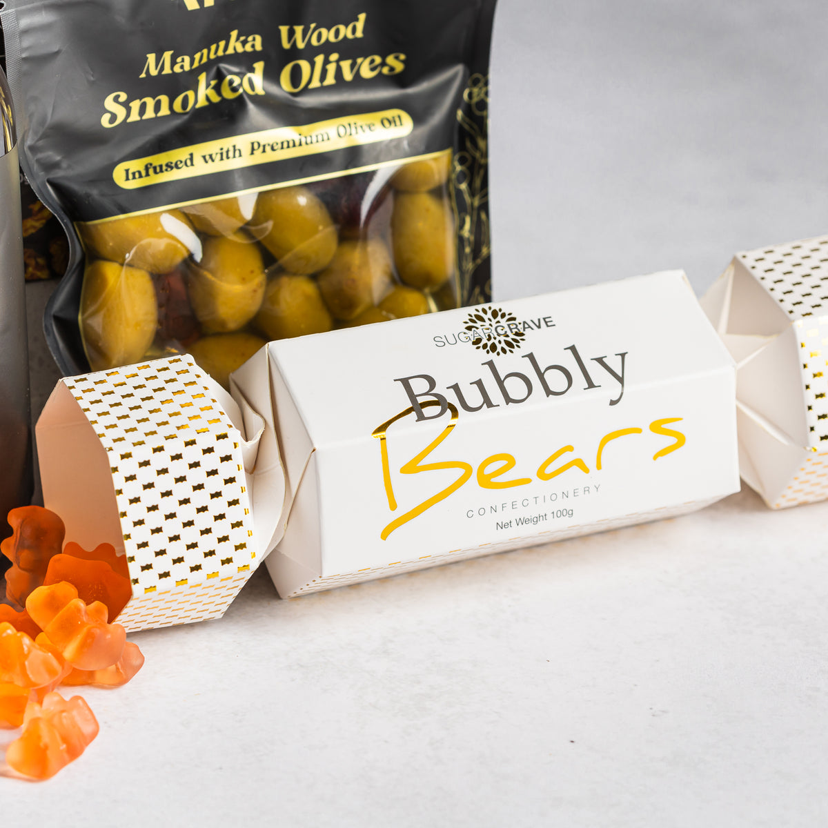 Bubbly Bears sweets spilling from a white and gold Christmas cracker beside a pouch of mānuka wood smoked olives