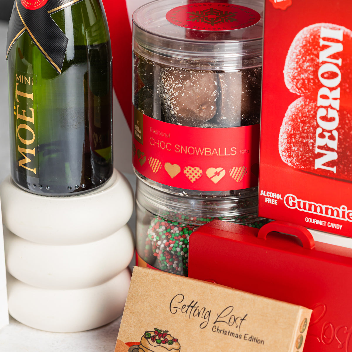 Mini Moët champagne beside stacked jars of chocolate snowballs and festive chocolate buttons, with Negroni gummies
