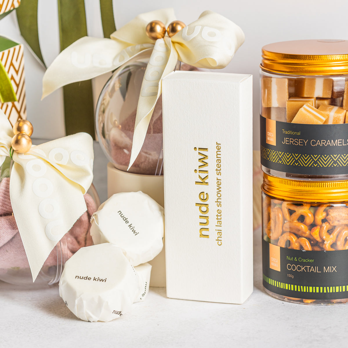 Nude Kiwi chai latte shower steamers beside ribbon-tied baubles and gold-lidded jars of caramels and cocktail mix
