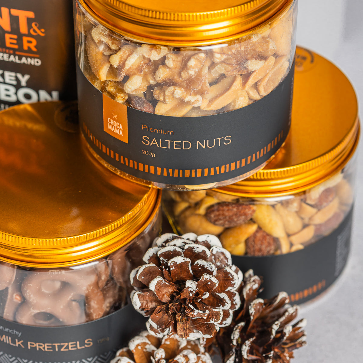 Gold-lidded jars of salted nuts, chocolate-coated pretzels and snack mix, styled with white-tipped pine cones.