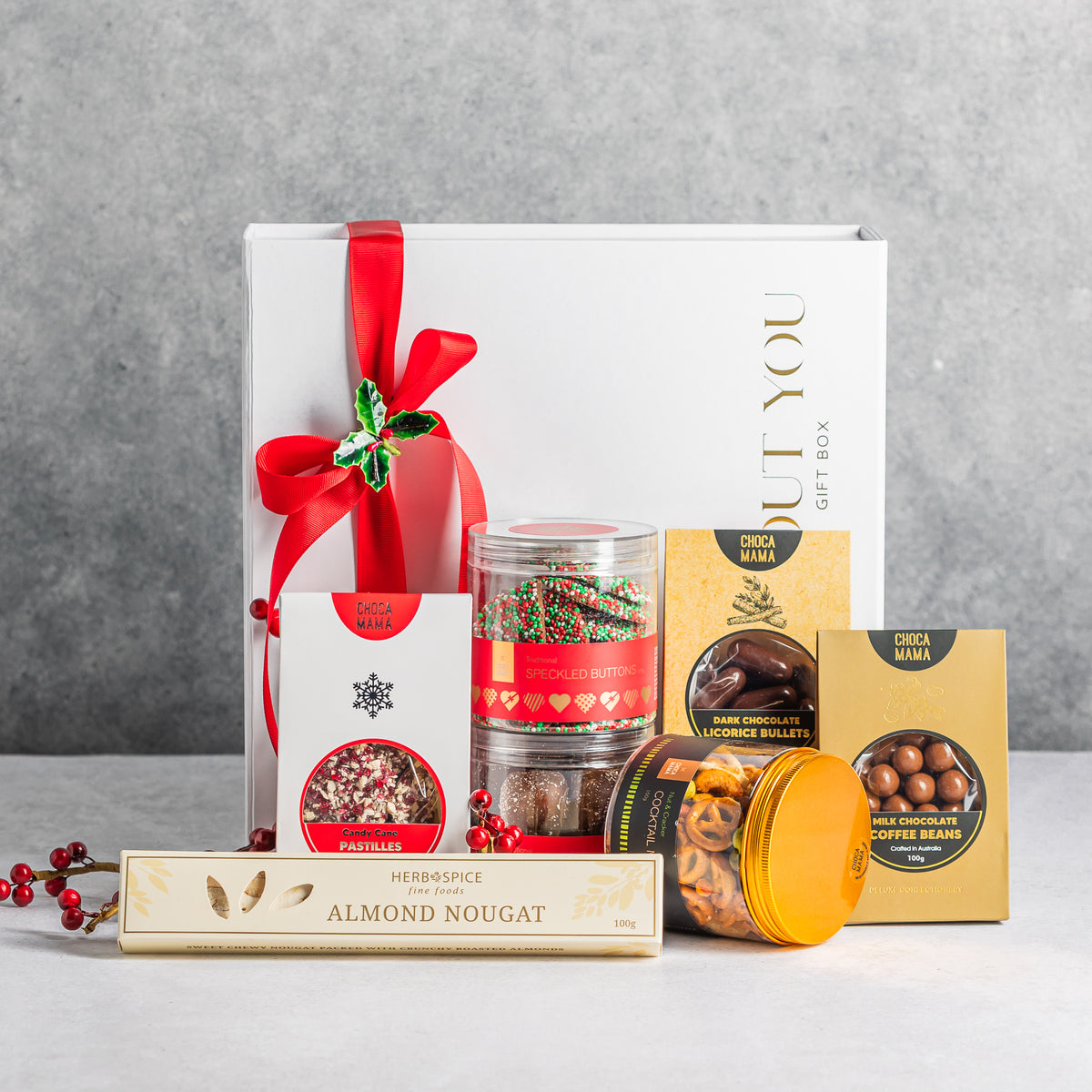 Christmas gift box with chocolate treats, almond nougat and cocktail snack mix, styled with red ribbon and holly.
