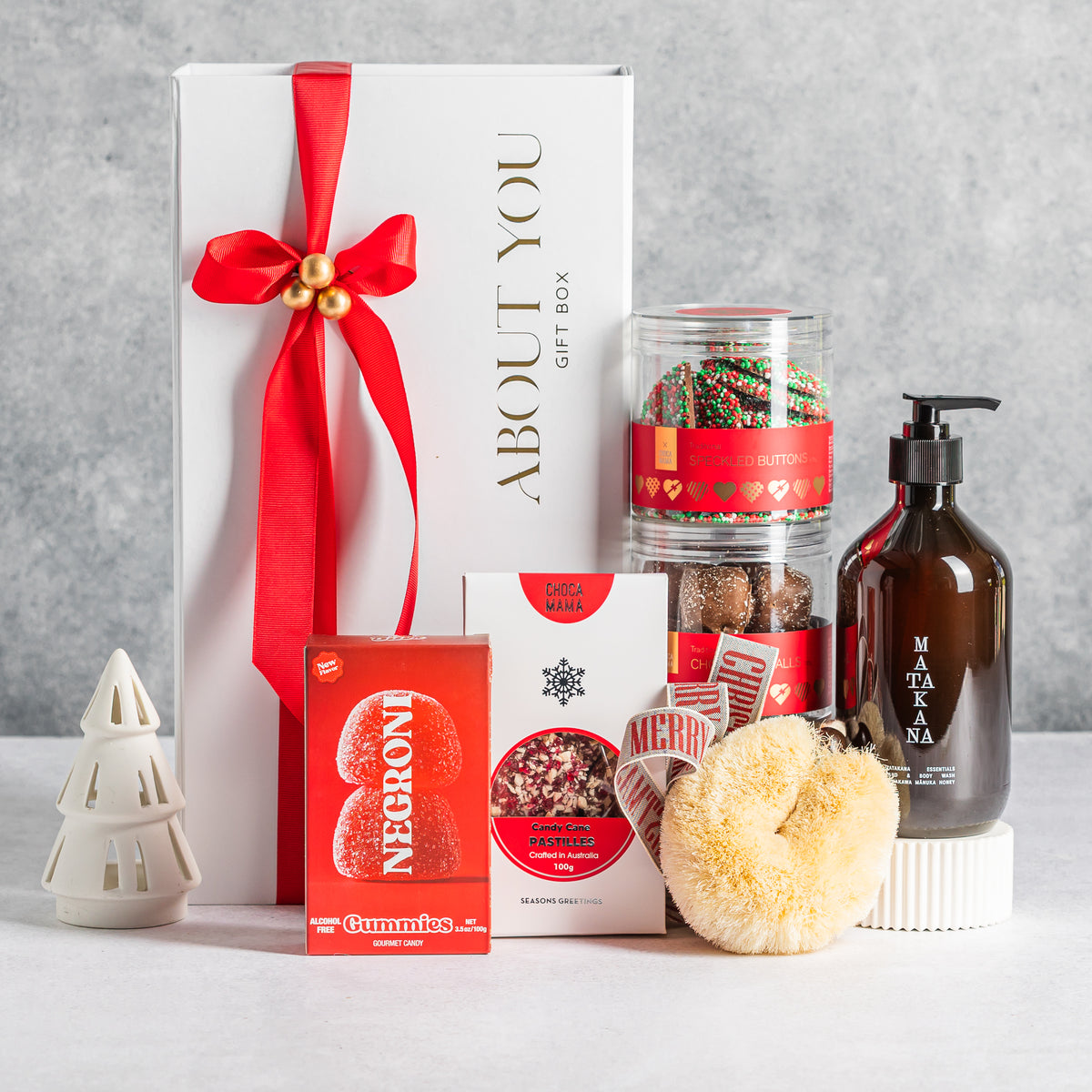 Christmas gift box with chocolates, Negroni gummies, a Matakana pump bottle and a bath sponge, styled with red ribbon.