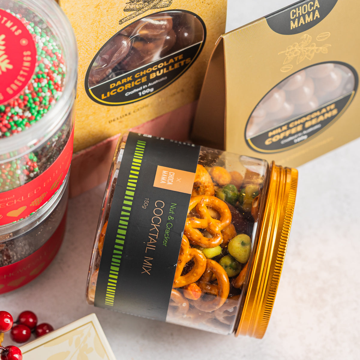 Gold-lidded jar of nut and cracker cocktail mix beside chocolate coffee beans, liquorice bullets and festive chocolate buttons.