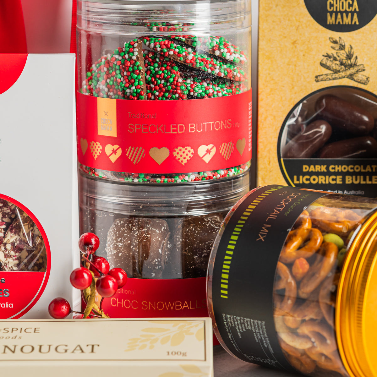 Festive speckled chocolate buttons and chocolate snowballs in stacked jars beside cocktail snack mix and liquorice bullets