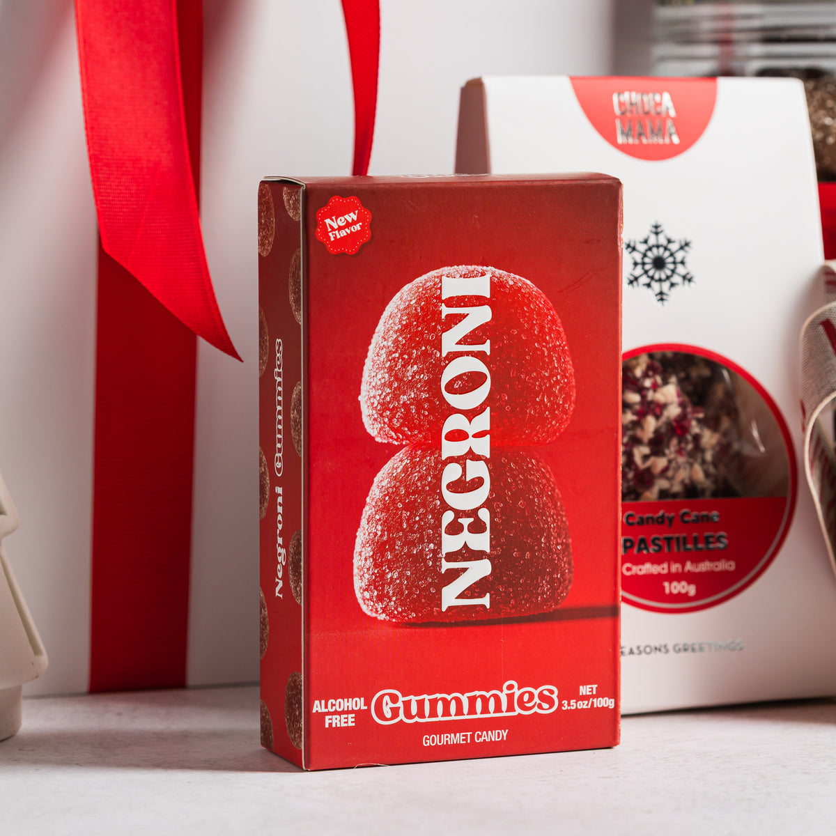 Alcohol-free Negroni gummies in red packaging beside Chocamama candy cane pastilles and a red-ribboned gift box