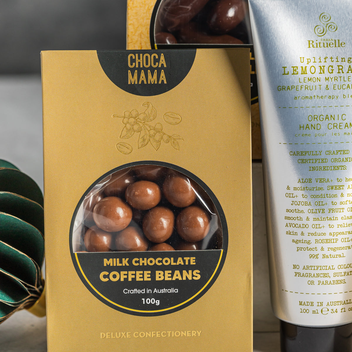 Chocamama milk chocolate coffee beans in gold packaging beside lemongrass hand cream and a green paper bauble