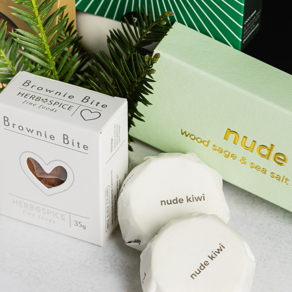 Nude Kiwi wood sage and sea salt shower steamers beside a Herb & Spice brownie bite and festive greenery