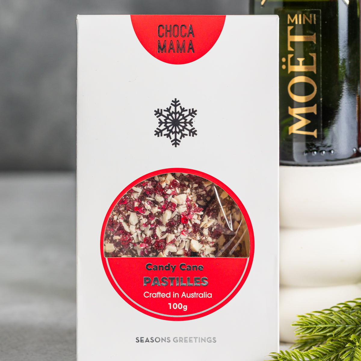 Chocamama candy cane pastilles in white and red snowflake packaging, with a mini Moët champagne bottle behind